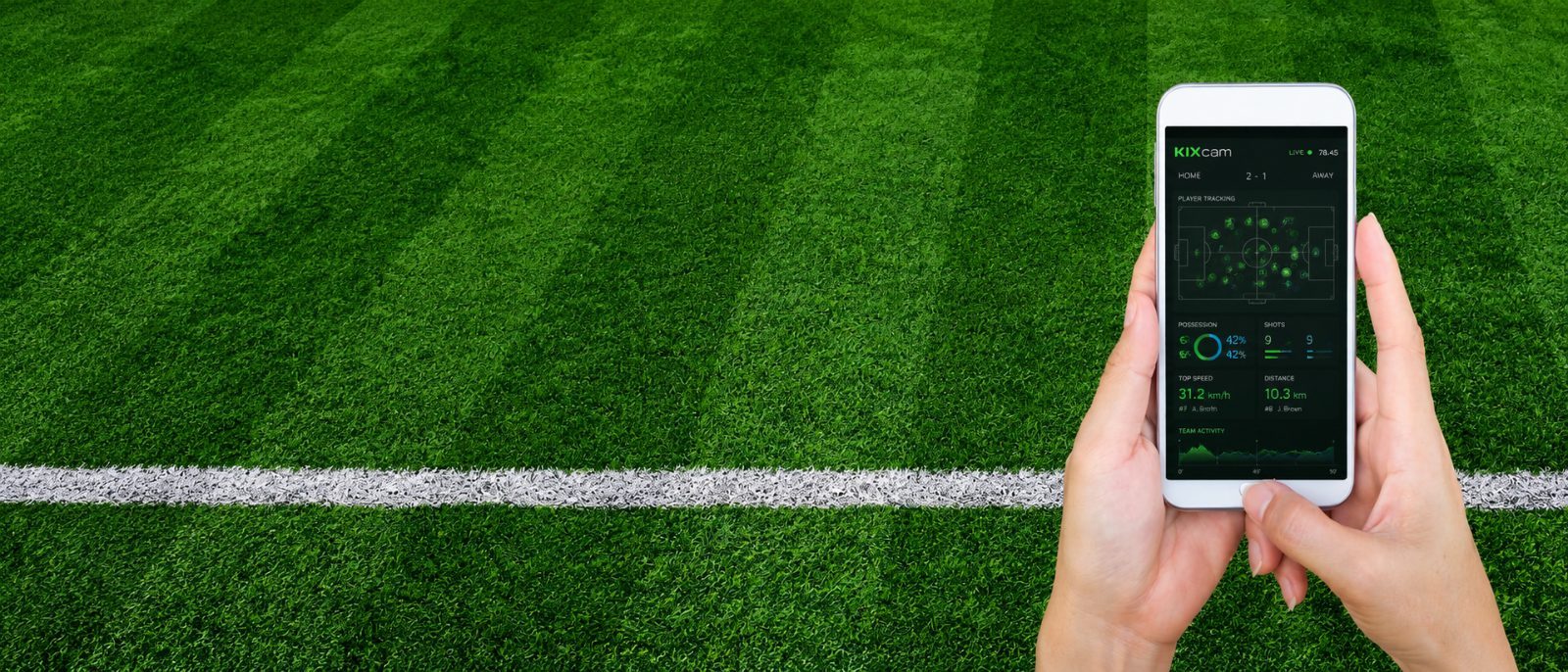 Hands holding a phone showing the KIXcam live tracking app over a striped turf field